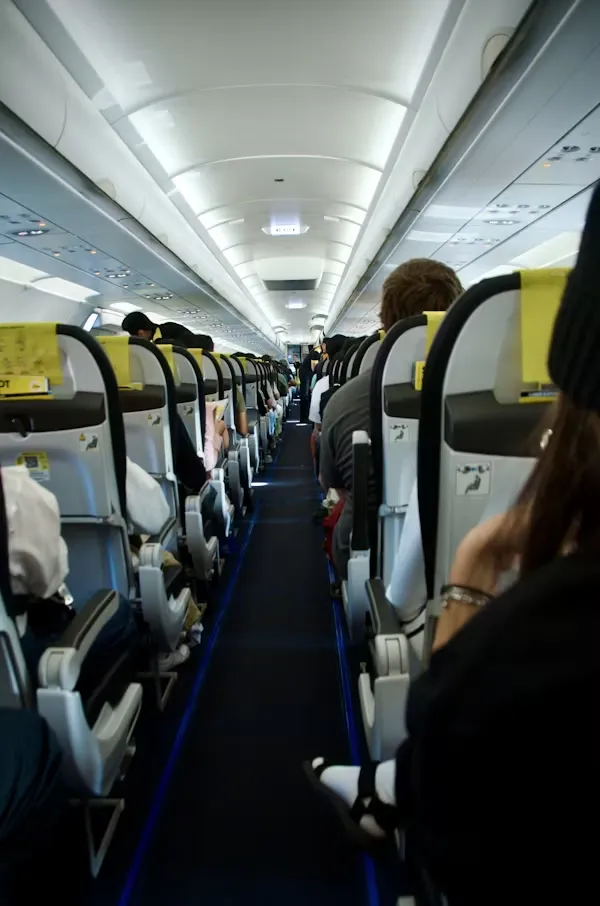 Passengers seated inside an airplane economy cabin with rows of seats and aisle visible
