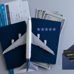 Model airplane placed over two passports with boarding passes and US dollar bills, symbolizing airline travel, loyalty programs, and flight-related expenses.