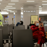 Airport waiting area with passengers using free Airport Wi-Fi on devices during a delay.