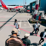 Passengers with backpacks walking across tarmac to board easyJet airplane via stairs, carrying devices with lithium batteries.
