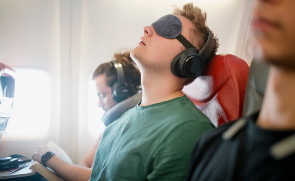 Guy resting in airplane seats using eye masks to manage red-eye flights sleep on overnight flights.