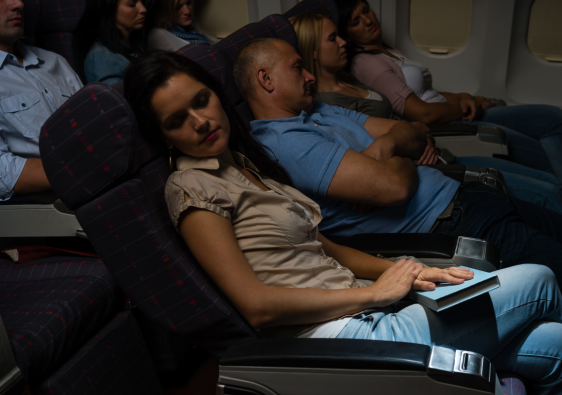 Multiple passengers sleeping in economy seats during red-eye flights sleep on overnight flights.