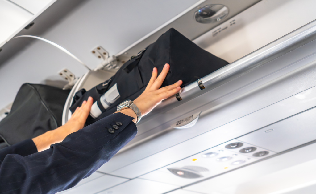 Hands adjusting a carry-on bag inside an airplane overhead bin.