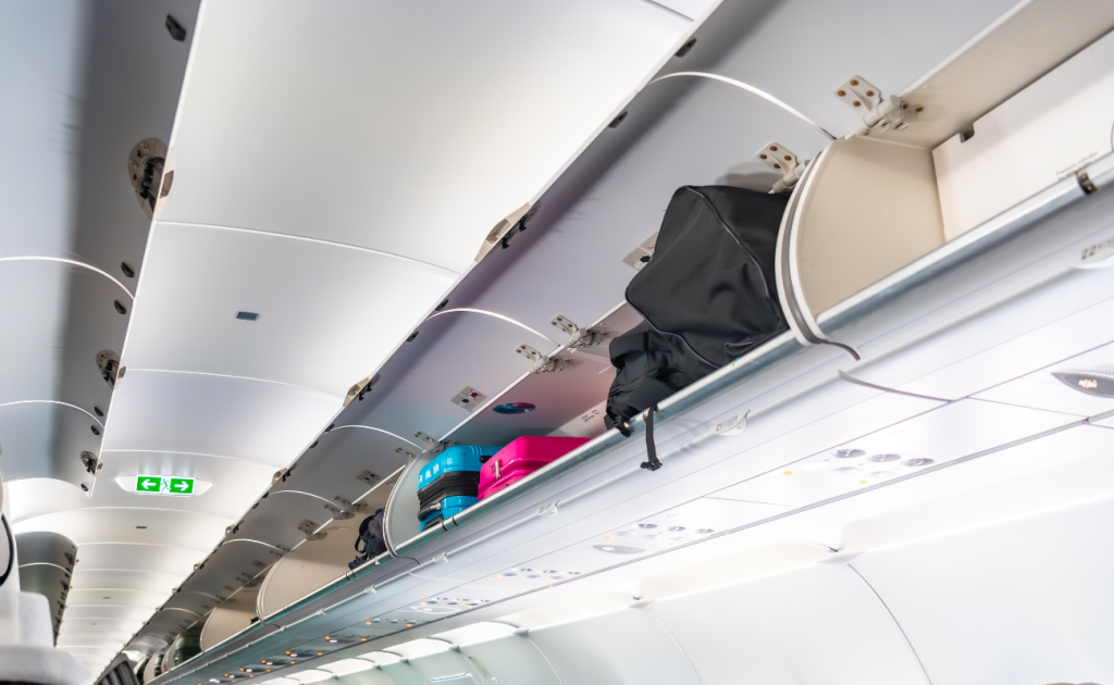 Business traveler looking at luggage stored in an airplane overhead bin.