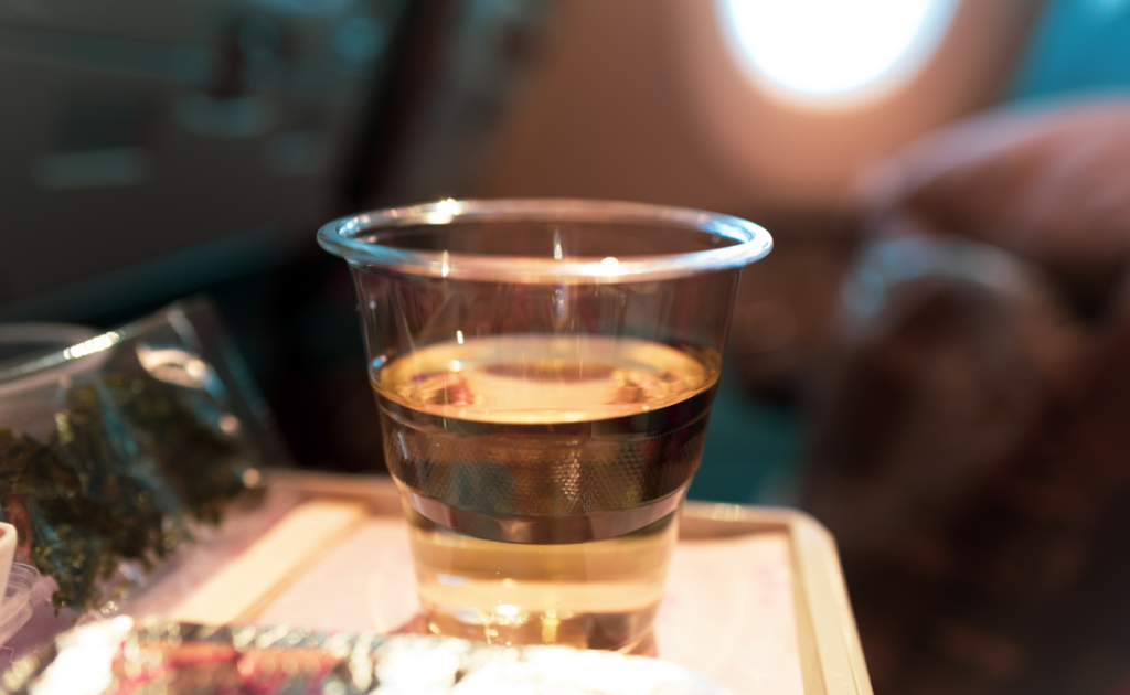 Plastic cup of alcoholic beverage served on an airplane tray table.