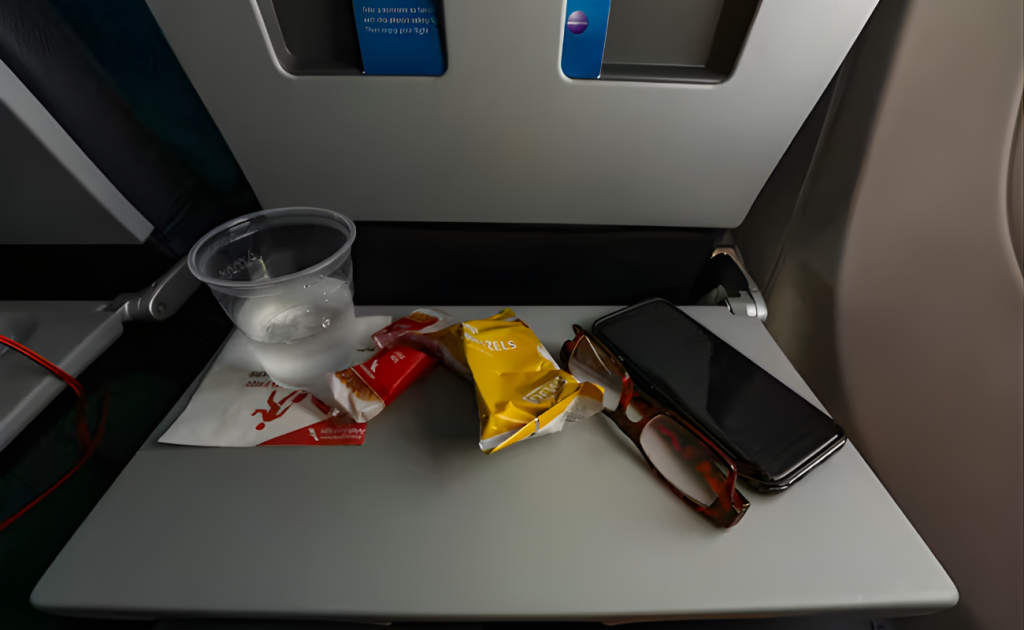Airplane tray table with water cup, pretzels, snack bar, glasses, and phone solid foods allowed after bringing through TSA.