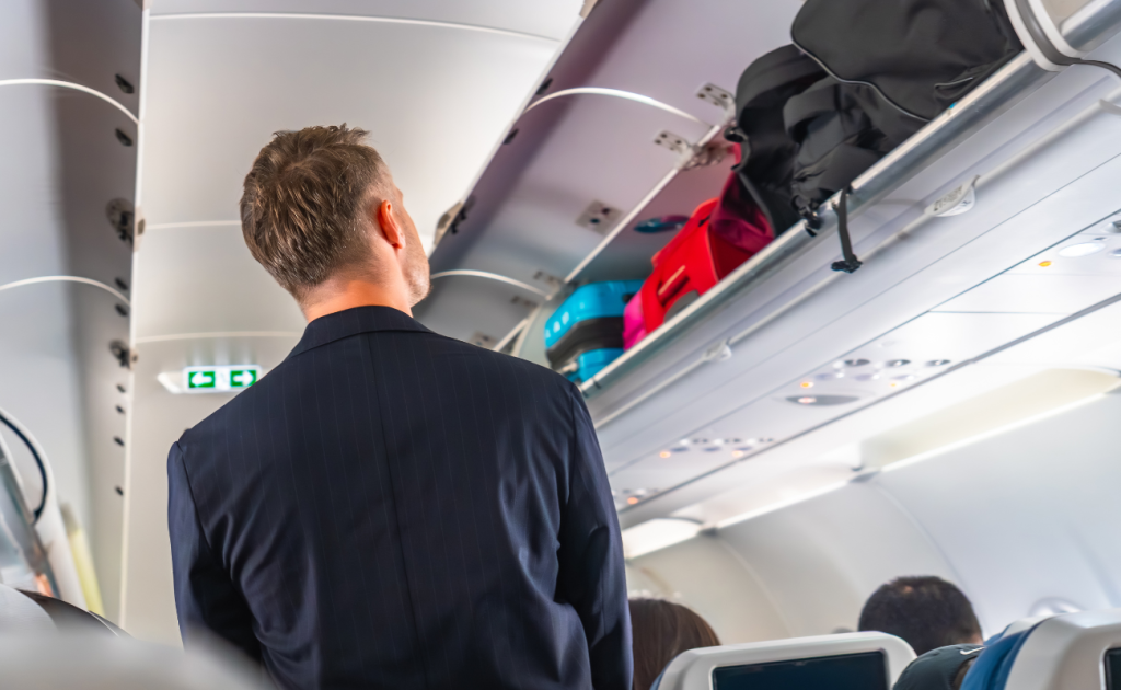 Airplane overhead bins filled with carry-on suitcases and personal items.