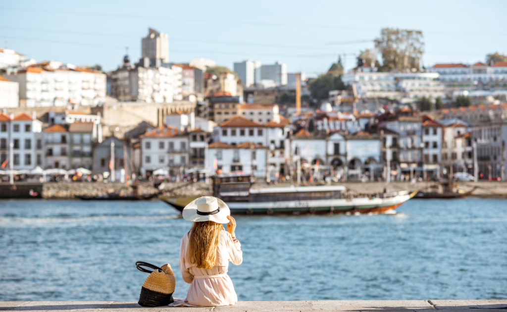 Solo traveler sitting by a riverfront in a European city, watching boats pass