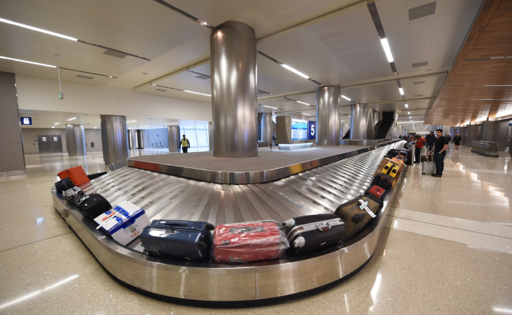 Checked luggage moving on an airport baggage claim carousel with travelers waiting nearby