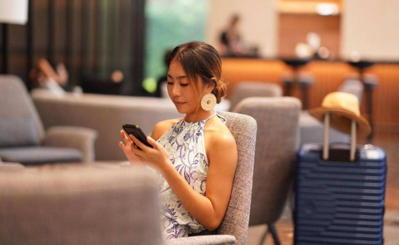 Passenger checking phone at airport while following 2026 airline check-in rules and deadlines.