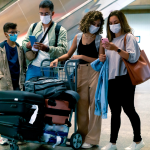 Travelers arriving early at the airport checking flight details before security screening.