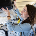 Woman placing a carry-on bag into an airplane overhead bin during boarding.