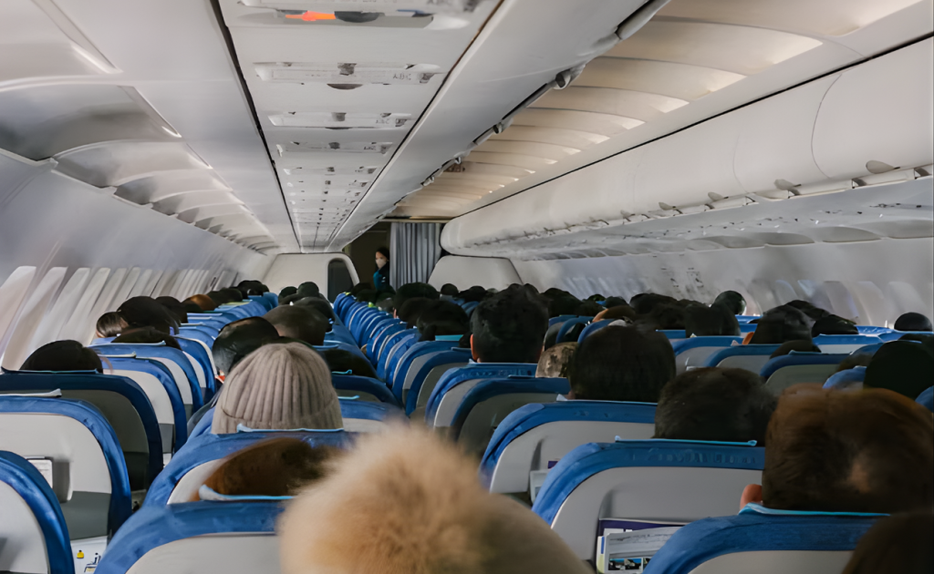 Passengers boarding a crowded airplane, stowing carry-on luggage in overhead bins on economy class.