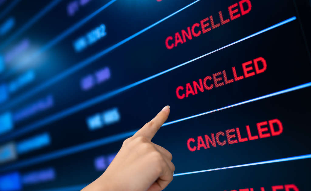 Passenger pointing at airport departure board showing multiple return flights cancelled