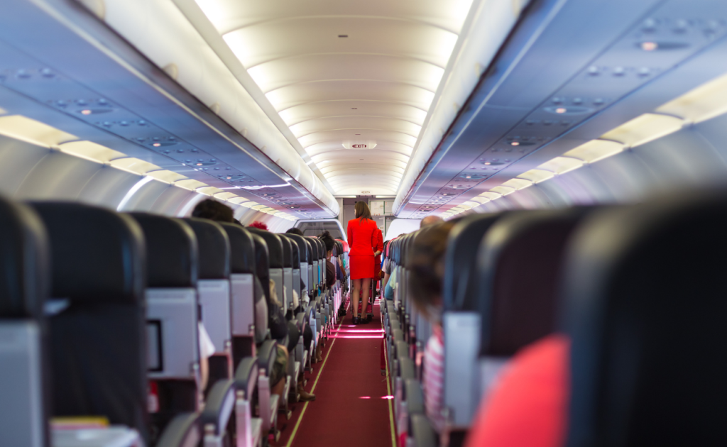 Flight attendant walking down airplane broken seat aisle during in-flight service